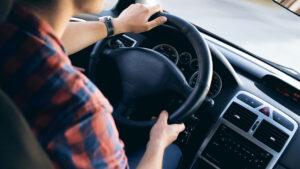 A person with a watch on their left wrist driving a car, with both hands on the steering wheel.