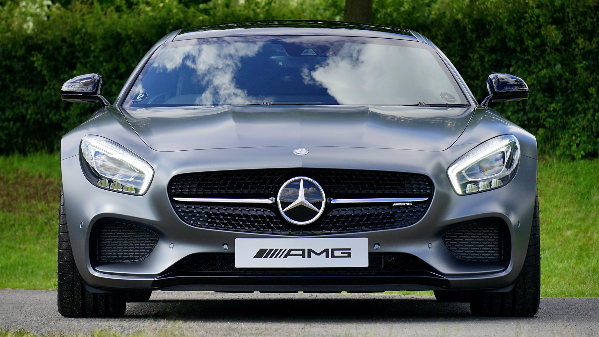 A gray Mercedes-AMG GT is parked outside with trees in the background.